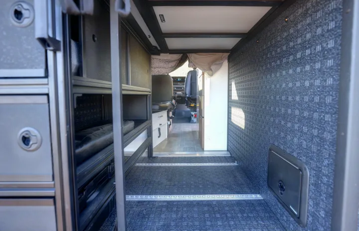 RV rental interior: modular storage, durable floor with cargo tracks, and a spacious layout leading to the front cabin area.. Mercedes-Benz Sprinter 2021