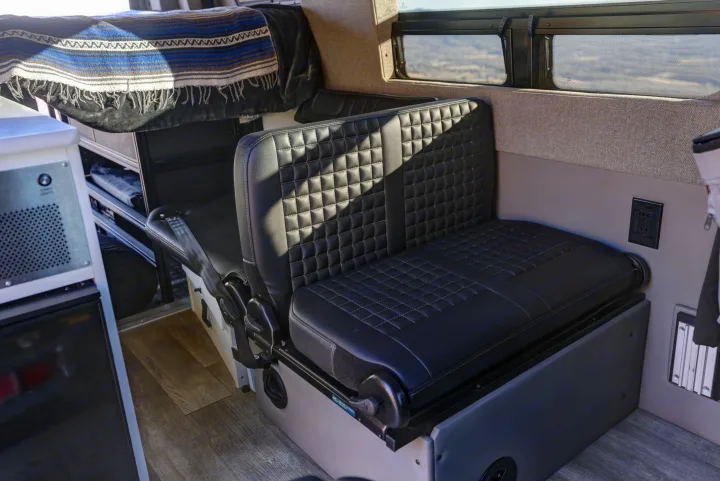 RV rental: Modern camper van interior featuring black quilted bench seats, a striped blanket, wood floor, and custom storage.. Mercedes-Benz Sprinter 2021