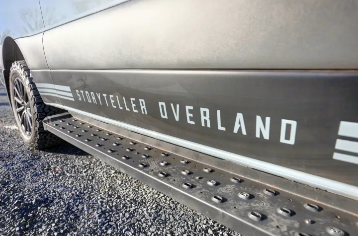 Storyteller Overland van's side, displaying "STORYTELLER OVERLAND" branding, rugged step, and all-terrain tire. Ideal for rv rental.. Mercedes-Benz Sprinter 2021
