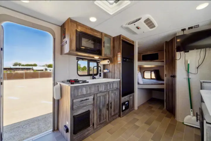 Inside this modern RV rental: a well-equipped kitchen, cozy bunk beds, and an open door view to the outdoors.. Forest River Salem FSX 2021