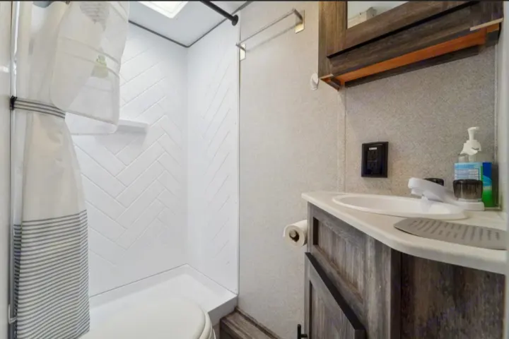 This RV rental bathroom features a compact shower with herringbone walls, a toilet, and a vanity with a sink.. Forest River Salem FSX 2021