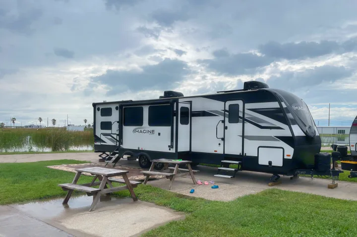 This spacious white & black RV rental is parked at a scenic campground site, featuring picnic tables, a pond, and palm trees.. Grand Design Imagine 3210BH 2023