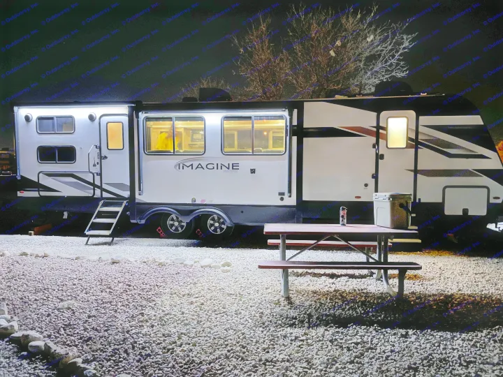Nighttime view of a brightly lit Grand Design "Imagine" rv rental, parked on a gravel lot with a picnic table.. Grand Design Imagine 3210BH 2023