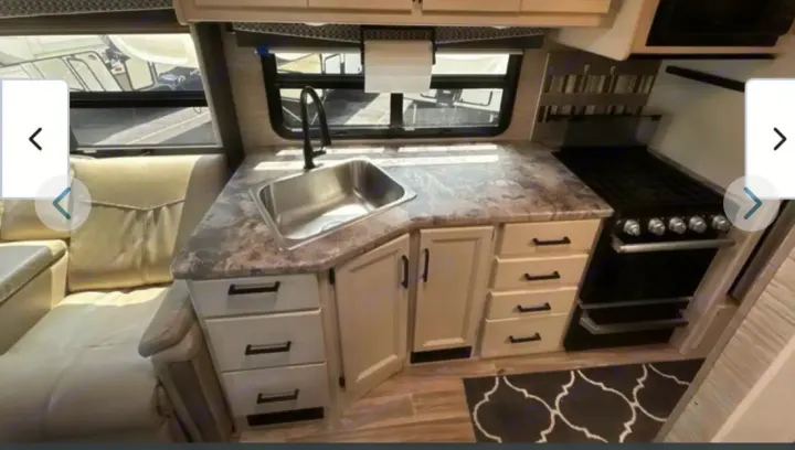 Modern rv rental interior: well-equipped kitchen with a sink, stove, light cabinets, and a comfy dinette.. Thor A.C.E. 2021
