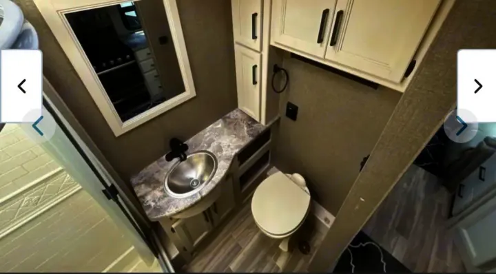 Compact RV rental bathroom featuring a vanity, sink, toilet, and storage cabinets. A mirror reflects the RV's kitchen.. Thor A.C.E. 2021