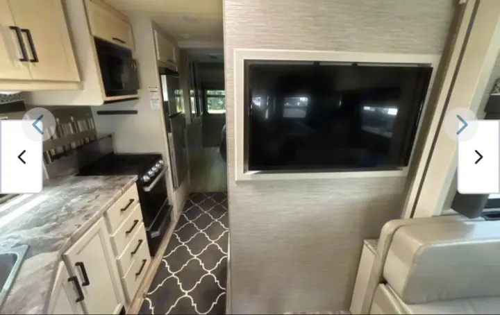 View inside a modern RV rental, showing the kitchen with stove, microwave, and counter, plus a TV and sofa.. Thor A.C.E. 2021