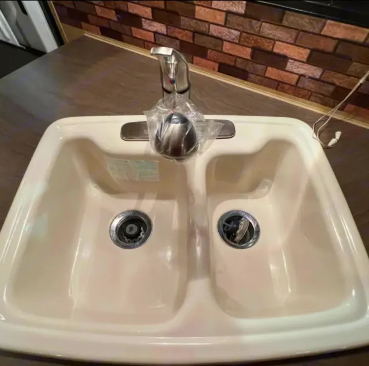 Clean cream-colored double sink with chrome faucet (covered in plastic) in an RV rental kitchen, ready for your camper journey.. Jayco Eagle 2014