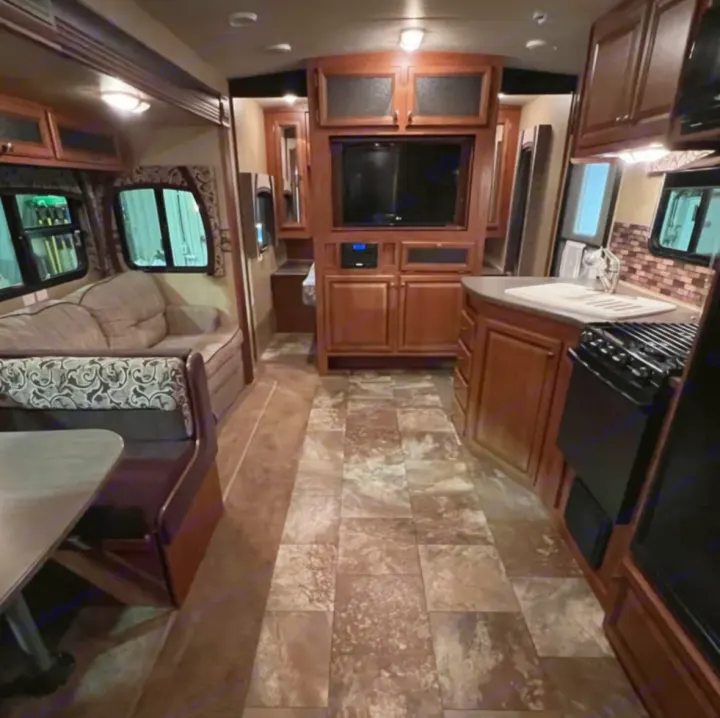 RV rental interior: cozy living area with dinette, entertainment center, & kitchen. Wood cabinets, tiled floor visible.. Jayco Eagle 2014