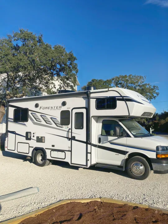 This white Forester RV rental, parked on a gravel driveway, features sleek black & gray stripes, ideal for a road trip.. Forester LE 2024