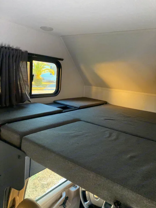 Spacious cab-over bunk sleeping area in an RV rental, offering comfortable accommodation with a view through the window.. Forester LE 2024