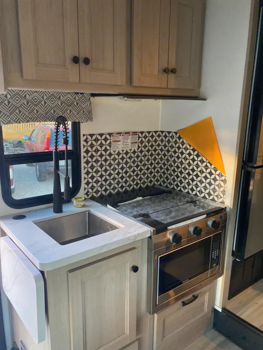 Detailed view of a modern RV rental kitchen, showing sink, stovetop, oven, microwave, and a black/white backsplash.. Forester LE 2024
