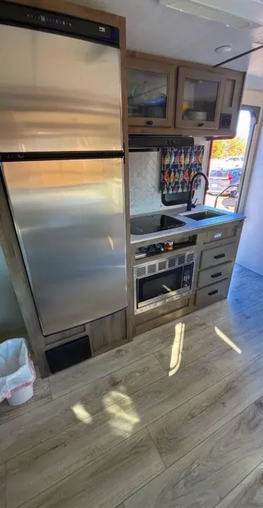 Modern RV rental kitchen: stainless steel fridge & microwave, gray counters, sink, wood-look cabinets & flooring visible.. Forest River Surveyor 2022