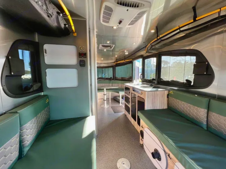 Explore this modern RV rental interior with green seating, a kitchenette, and panoramic windows. Ideal for comfortable travel.. Airstream Basecamp 2022