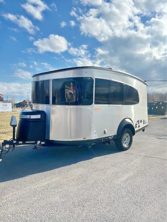 A sleek silver Airstream Basecamp travel trailer, ideal for an rv rental adventure. Parked on asphalt under a blue sky.. Airstream Basecamp 2022