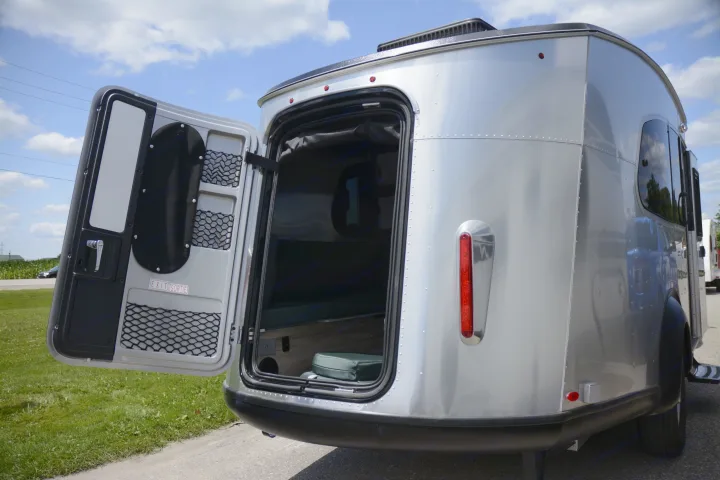 A silver compact RV rental, seen from the rear with its door open, revealing a cozy interior for travel adventures.. Airstream Basecamp 2022