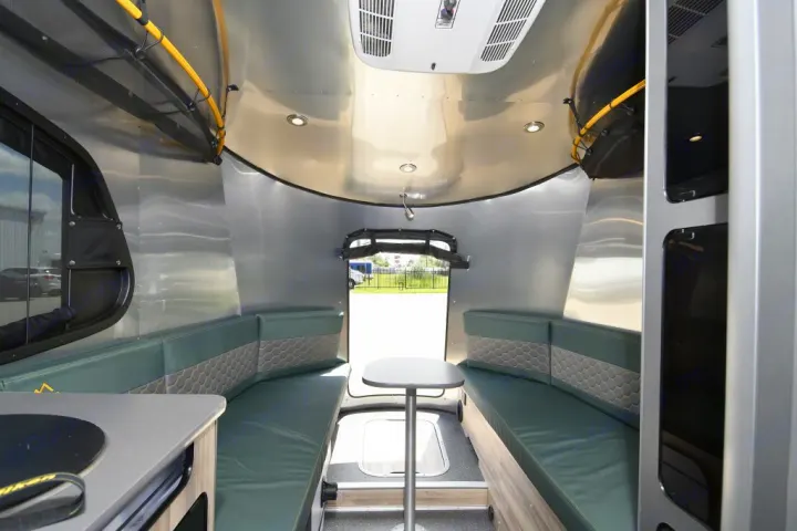 Step inside this compact rv rental, featuring green upholstered benches, a dining table, and a rear exit for your travel adventures.. Airstream Basecamp 2022