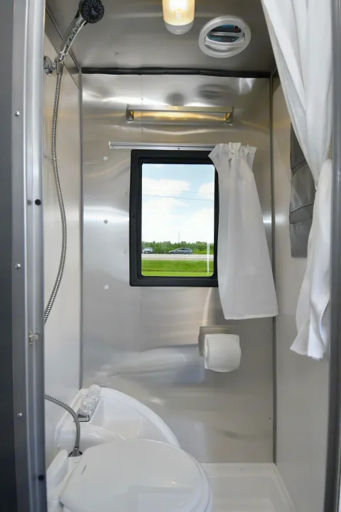 RV rental: compact wet bath interior with shower, toilet, sink, and window view showing a road outside.. Airstream Basecamp 2022