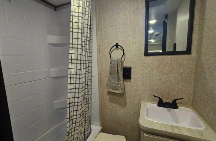 This RV rental bathroom features a compact white shower, plaid curtain, sink with black faucet, mirror, and toilet.. Jayco Jay Flight SLX 2026
