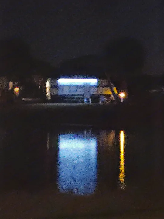 Grainy night view of an RV rental with bright blue and orange lights, reflected in dark water.. Forest River Salem Cruise Lite 2021