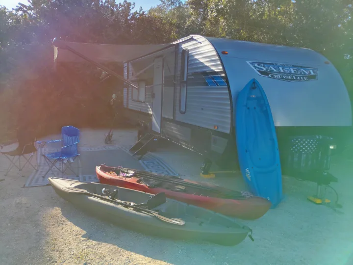 RV rental getaway: a travel trailer with awning, three kayaks (blue, red, green), and camping chairs ready for adventure.. Forest River Salem Cruise Lite 2021