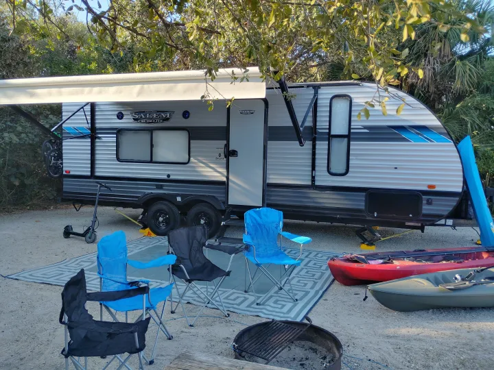 Campsite setup with an RV rental, chairs, fire pit, kayaks, and scooter, ready for outdoor adventure.. Forest River Salem Cruise Lite 2021