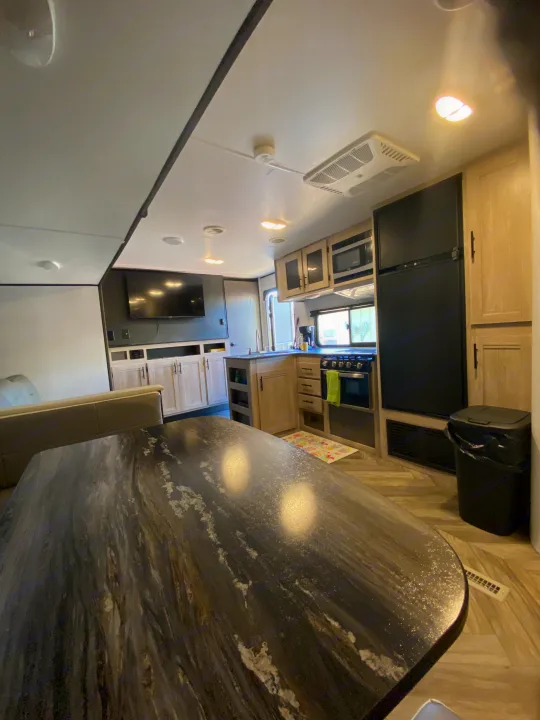 Modern RV rental interior: large dining table, full kitchen, and living area with TV. Ready for adventure!. Keystone RV Cougar 2022
