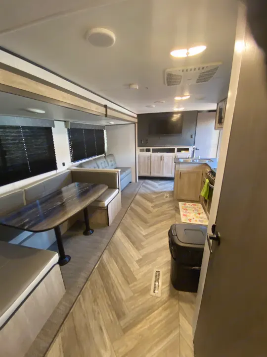 Bright RV rental interior featuring a dinette, living room with TV, and kitchen with modern herringbone flooring.. Keystone RV Cougar 2022