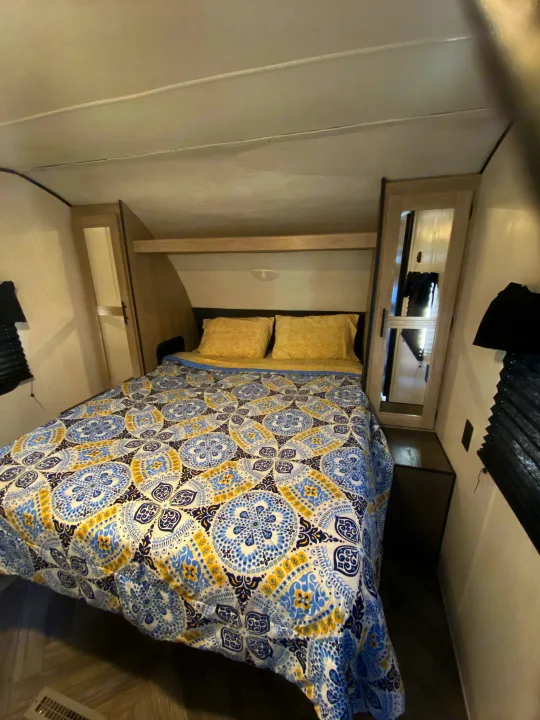 Inside a comfortable **rv rental** bedroom, featuring a vibrant blue, yellow, and white patterned bedspread and convenient bedside storage.. Keystone RV Cougar 2022