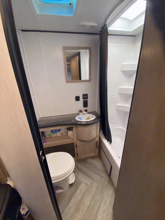 Compact RV rental bathroom with toilet, sink vanity, and shower stall. A skylight brightens this functional space.. Keystone RV Cougar 2022