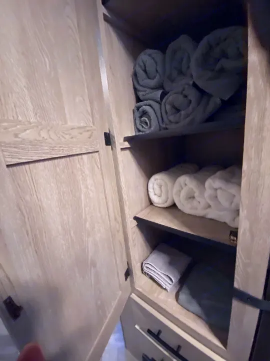 Organized storage in an RV rental: shelves filled with neatly rolled gray and white towels in a light wood cabinet.. Keystone RV Cougar 2022