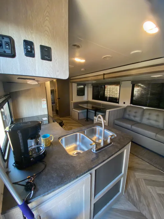 Spacious RV rental interior featuring a modern kitchen with a dual sink and coffee maker, plus a cozy dinette and sofa.. Keystone RV Cougar 2022
