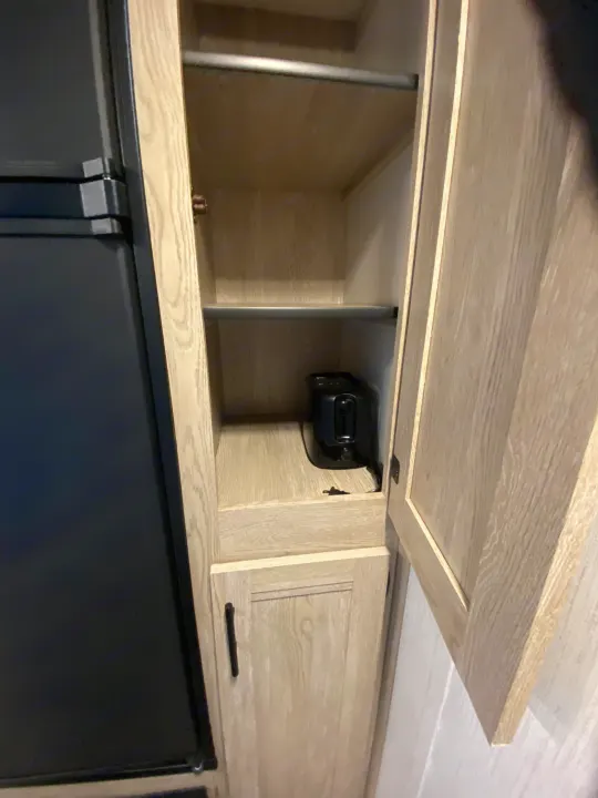 Inside an RV rental's light wood pantry cabinet: a toaster on a shelf, with a clothing rod above and a fridge to the left.. Keystone RV Cougar 2022