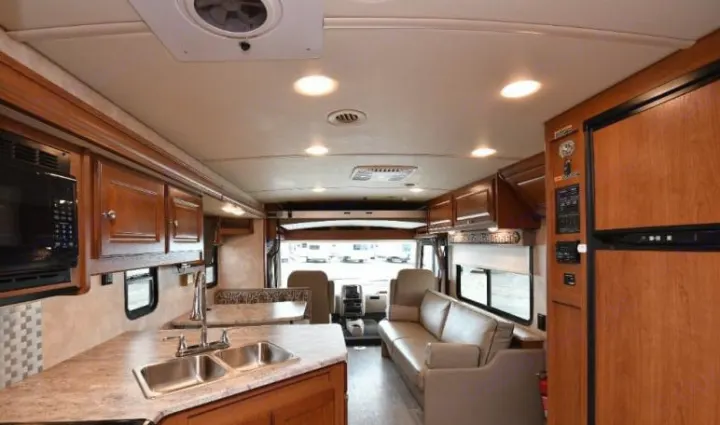 Spacious RV rental interior. Features a modern kitchen with a microwave, sink, wood cabinets, and a comfortable living area with sofa.. Winnebago Vista 2019