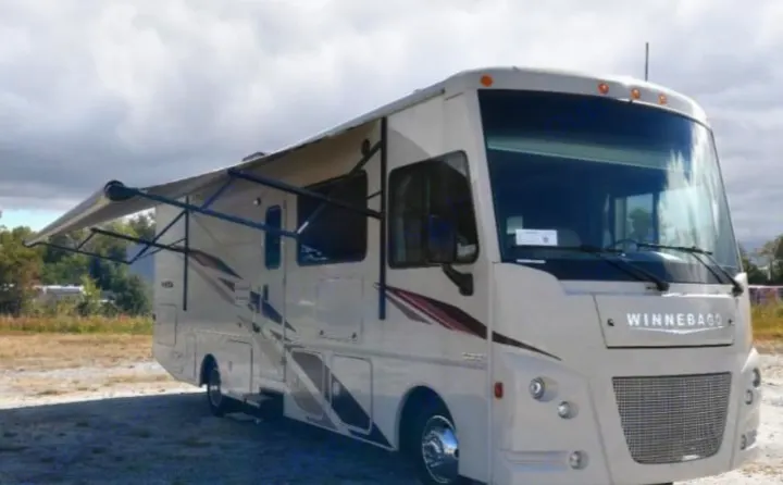 Cream-colored Winnebago RV rental with an extended awning, parked outdoors. Perfect for your next adventure.. Winnebago Vista 2019