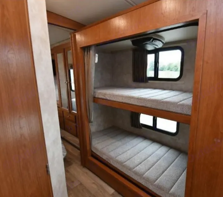 Inside an RV rental: cozy bunk beds with windows, an AC unit, and nearby storage. Ideal for family adventures.. Winnebago Vista 2019
