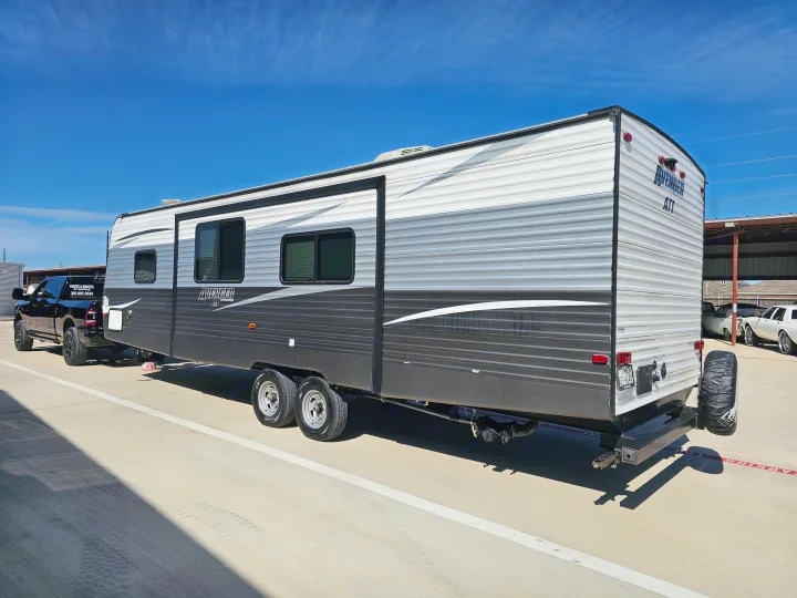 A black pickup truck tows a large grey and white Avenger RV rental, parked on concrete under a bright blue sky.. Avenger ATI 2019