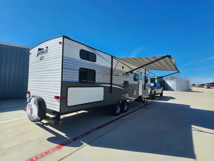 Avenger ATI travel trailer RV rental, with an extended awning, parked on a sunny lot next to a truck.. Avenger ATI 2019