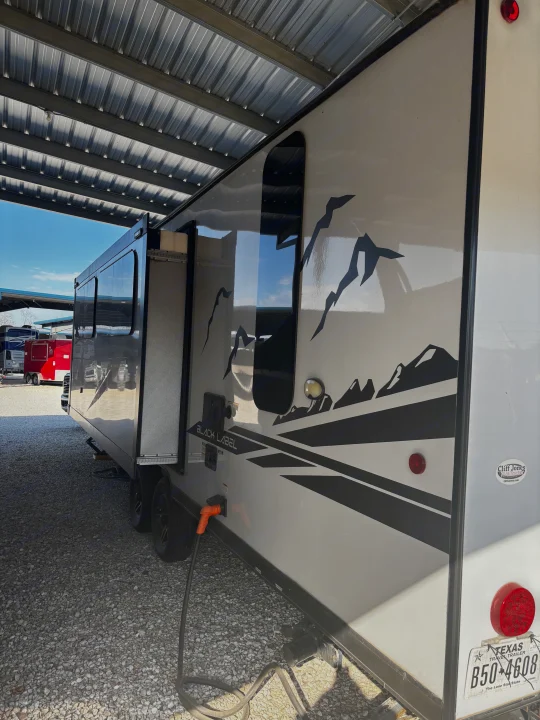 A white travel trailer RV rental with black mountain graphics and "BLACK LABEL" branding, parked under a metal canopy.. Forest River Cherokee Grey Wolf 2022