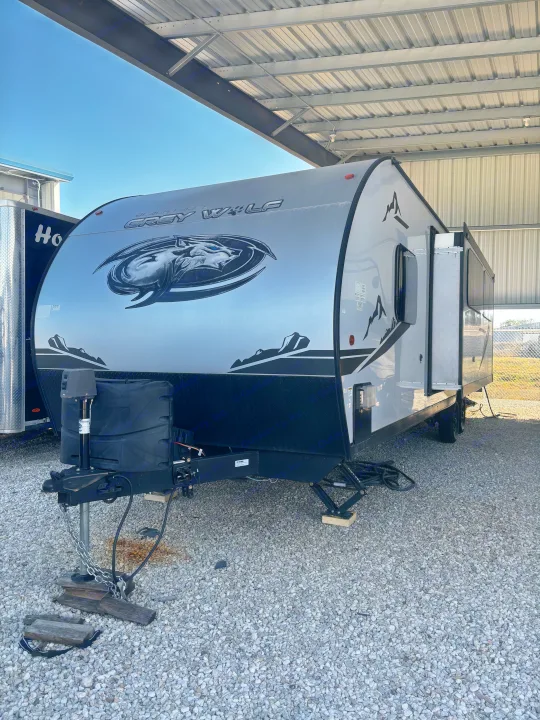 Grey Wolf rv rental travel trailer. Silver and black camper parked on a gravel lot under a metal canopy, ready for adventure.. Forest River Cherokee Grey Wolf 2022