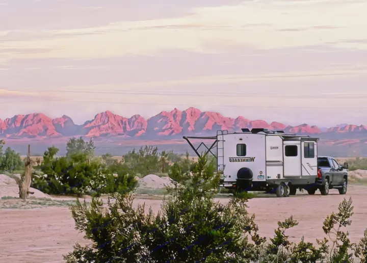 RV rental adventure: a white travel trailer & truck parked in a scenic desert with glowing pink mountains.. Winnebago Minnie 2201MB 2022