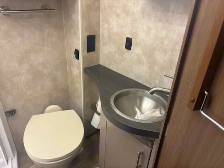 This RV rental bathroom provides a compact toilet, stainless steel sink, and counter, ideal for your journey's comfort.. Itasca Navion 2019