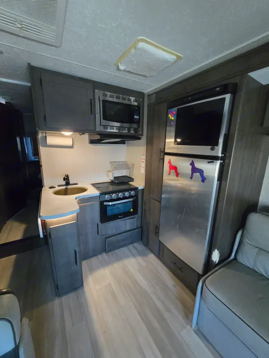 Cozy rv rental kitchen featuring a stainless steel microwave, stove, sink, and full-size refrigerator. Modern cabinetry.. Forest River Coachmen Leprechaun Premier 2022