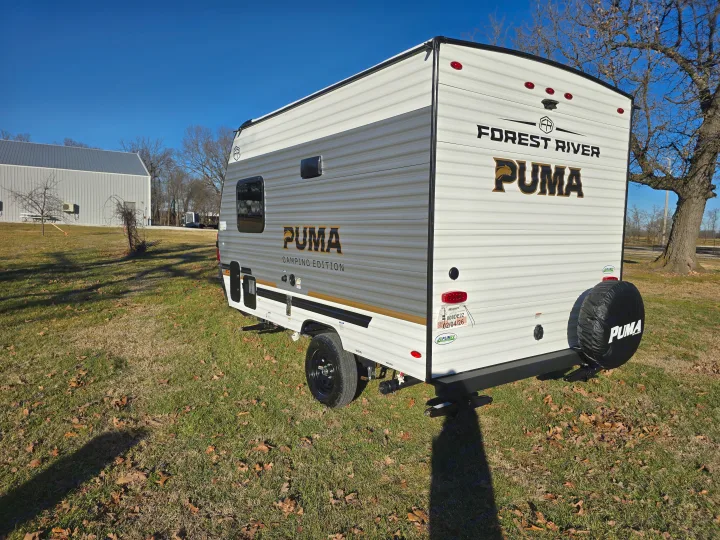 A white Forest River Puma Camping Edition travel trailer, perfect for an rv rental, sits on grass under a clear blue sky.. Palomino Puma Camping Edition 122BHCE 2026