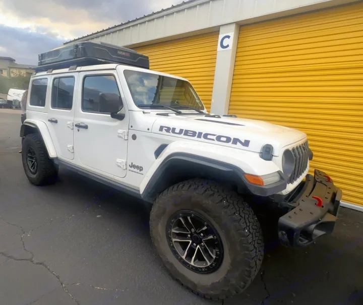 White Jeep Rubicon with a roof tent, an adventure-ready rv rental, parked by yellow storage units.. Jeep Wrangler Rubicon X 2024