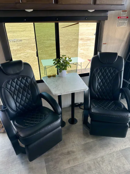 Cozy RV rental interior featuring two black quilted chairs, a small table with a plant, and a scenic outdoor view.. Genesis Supreme Powerlite LE Toy Hauler 2022