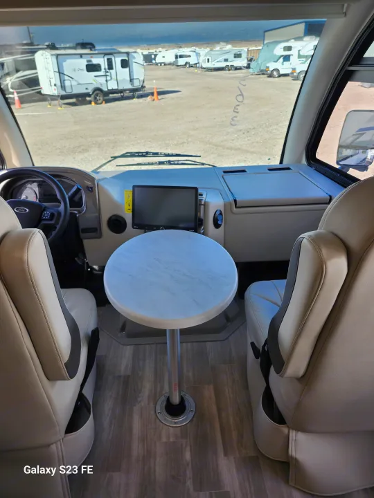 RV rental interior: front cockpit with swivel seats, a small table, and a view of other RVs parked outside.. Axis 24.1 2027