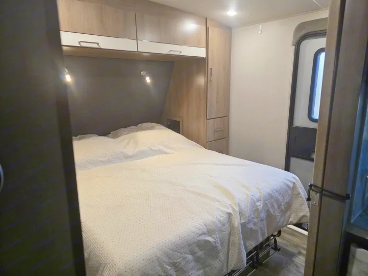 Inside an rv rental: a cozy bedroom with a neatly made bed, overhead cabinets, built-in wardrobe, and an exit door.. Grand Design Imagine 2022