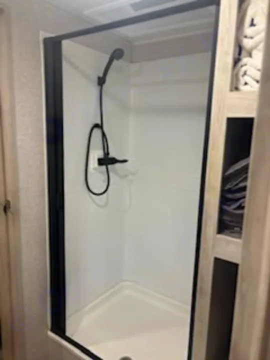 Compact, modern RV rental shower. Features a sleek black frame, white walls, and black fixtures for comfortable travel and camping.. East to West Della Terra 2023