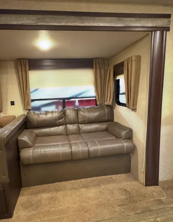 Explore this RV rental's comfy living space: a taupe sofa, windows with light curtains, and warm overhead lighting.. Forest River Cherokee 2017