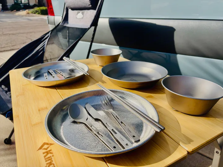 Outdoor dining: Titanium plates, bowls, and cutlery on a bamboo table, set up beside an rv rental.. Thor Synergy 2022